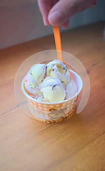 Ice cream on a wooden table. Hand holding an orange spoon