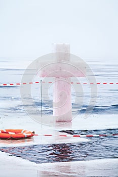 Ice cross and hole in winter pond on Epiphany