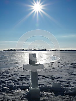 Ice cross near the hole on the background of bright blue sky and endless frozen river