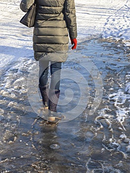 Ice-crusted ground, a woman walking on a slippery street, spring weather. Icy conditions