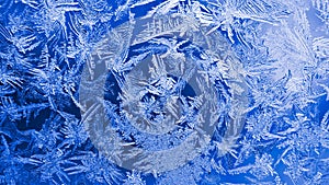 Ice crystals close-up on a window glass in winter. Dark blue and white background or wallpaper. Mystical fabulous abstract pattern