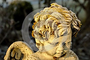 Ice crystals forming on green moss on a cute stone angel sculpture