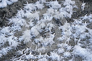 Ice crystals forming spike shapes on frozen river and sand, closeup macro detail