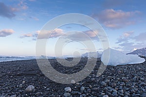 Ice cube breaking on black rock beach with blue sky background