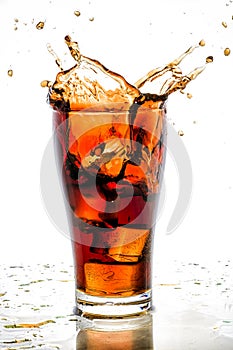 Ice cube droped in cola glass and cola splashing