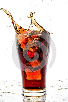 Ice cube droped in cola glass and cola splashing