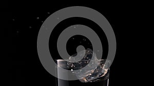 Ice cube falling into glass of water on black background