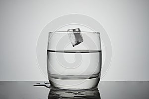 An ice cube falls into a glass of clear water. Liquid cooling concept