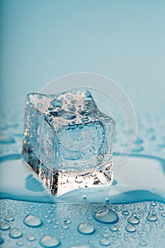 Ice cube with water drops on a blue background. The ice is melting