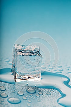 Ice cube with water drops on a blue background. The ice is melting