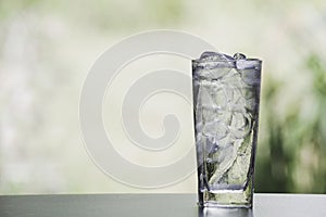 Ice cube and water in the glass on table with nature background