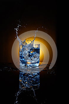 Ice cube and water splash in a clear glass.