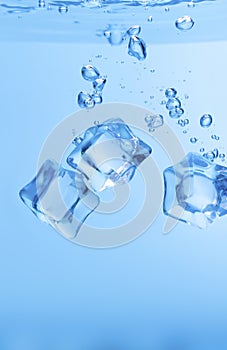 Ice cubes in blue water create bubbles that float to the surface