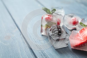 Ice cubes with different berries and mint on wooden table, closeup. Space for text
