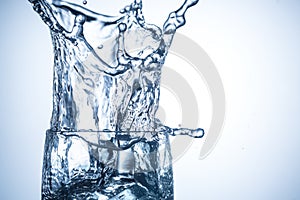 Ice cubes falling in glass with water splashes close up