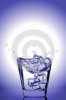 Ice cubes splashing into glass, ice cube dropped into glass of water, fresh, cold water, isolated on blue, caribian blue backgrou photo