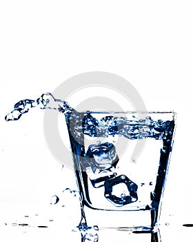 Ice cubes splashing into glass, ice cube dropped into glass of water, fresh, cold water, isolated on white, blue, caribian blue ba photo