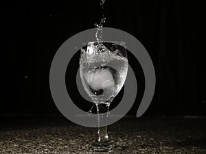 Ice falling on a glass with drink that spills and splashes.