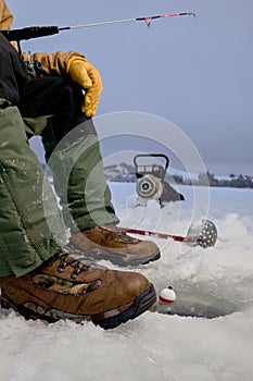 Ice fisherman fishing in ice hole and equipment