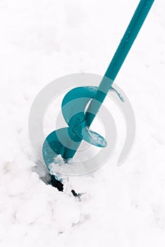 Ice fishing auger, lying on snow, used to drill holes in ice for winter fishing