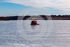 Ice fishing; frozen lake surface in winter with a red ice shanty or ice hut on the lake.