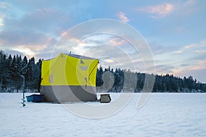 Ice fishing tent on a frozen lake at sunset. Fisherman camp on a peaceful winter evening