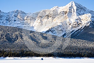 An ice fishing tent sits on a frozen mountain lake in the Canadian Rocky Mountains