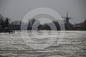 Ice flakes on river Hollandse IJssel at nieuwerkerk aan den IJssel during winter in the Netherlands with windmill