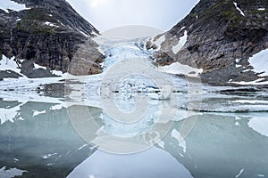Ice front of norwegian glacier Steindalsbreen surrounded by high mountains mirroring in the glacial lake with little icebergs