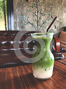 Ice green tea milk in glass on the wooden table with brown armchair background