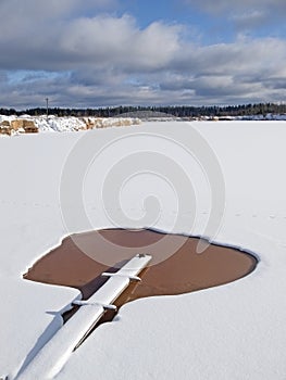 An ice-hole with brown water midst the snows. Winter landscape