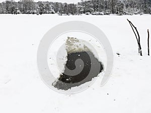 ice hole in frozen lake and view of park in winter
