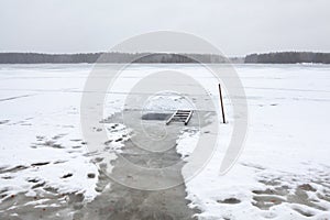 Ice-hole on lake for winter swimming. Wooden stair and shovel for ease of use