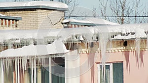 Ice icicles and snow hang from the roof of a house in winter. Danger of falling icicles, frosty day