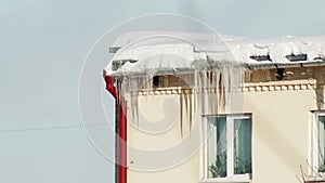 Ice icicles and snow hang from the roof of a house in winter. Danger of falling icicles, frosty day