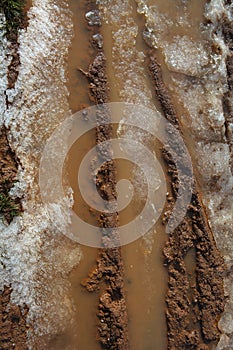 Ice on mud red clay soil road with tyres lines