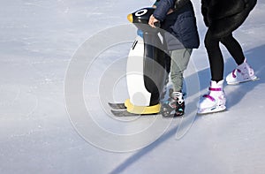 Ice rink. Mom teaches a child to skate. A boy holds a penguin for support. Winter family activities and sport concept