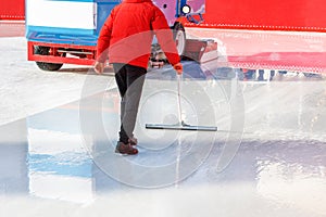 An ice rink worker cleans and levels the ice surface with a rubberized scraper