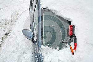 Ice scraper and brush for clearing automobile is on the hood of the car. Snow removing from car after blizzard. Partially cleaned