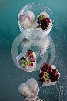 ice in the shape of a heart with red fragrant roses frozen in ice on a blue-green mirror background with water drops