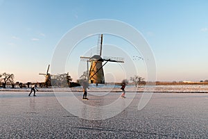 Ice skaters on a frozen windmill canal at sunrise moment