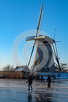 Ice skaters on a frozen windmill canal at sunrise moment