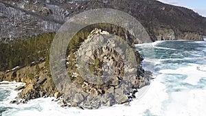 Ice and snow on a frozen river and the rocky forested shore from a height. Clip. Aerial view of the mountains covered by