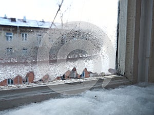 Ice, snow and frozen water crystals on glass. Window with double wooden frames. Outside the window is a street and a