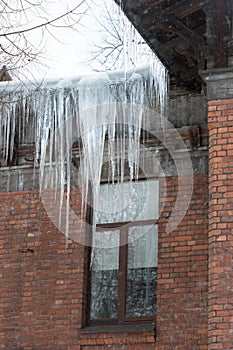 Ice stalactite hanging from the roof with wooden wall. Building covered with large icicles