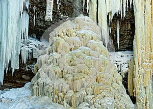 Ice stalagmite and many icicles in the stone well of the waterfall.