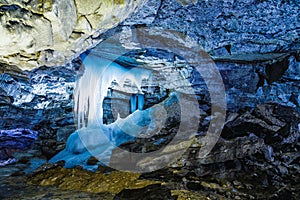 Ice stalagmites in blue light fantastic in a beautiful cave with numerous mining deposits