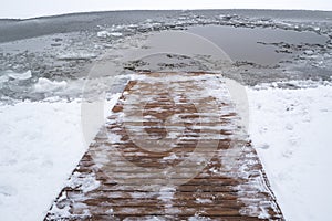 Ice swimming place with a snow-covered wooden path descending into the water