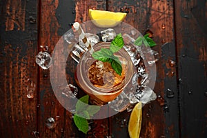 Ice tea with lemon slices and mint in glass jar, on rustic wooden background