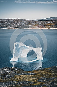 Iceberg with an arch in Antarctic Greenland waters against the backdrop of the mountains of the Arctic Peninsula. Small